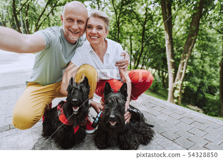 Smiling adult couple with two black dogs in park 54328850