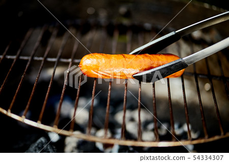 Juicy sausage on hot grill with tongs during summer barbecue Juicy sausage on hot grill with tongs during summer barbecue 54334307