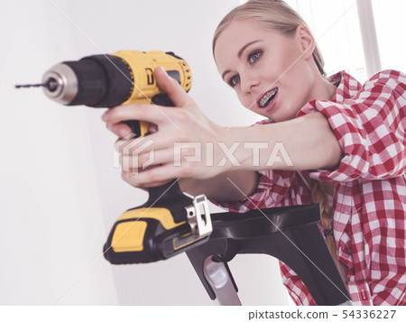 Woman using drill on ladder Woman using drill on ladder 54336227