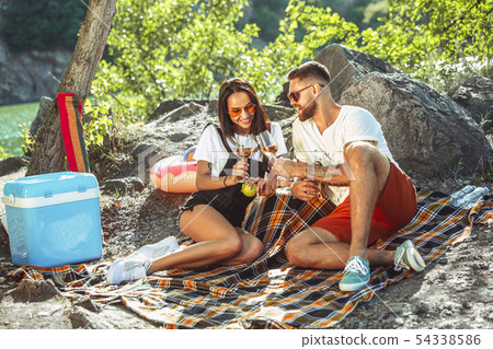 Young couple having picnic at riverside in sunny day Young couple having picnic at riverside in sunny day 54338586