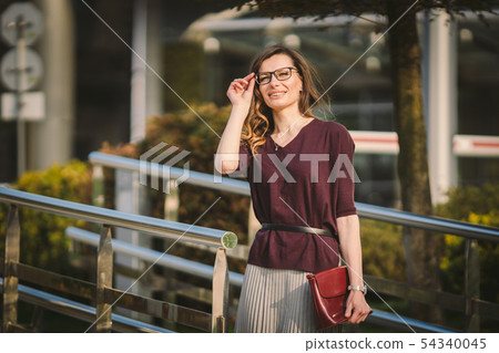 Caucasian adult lady woman in glasses posing near office building outside. Business lady in skirt 54340045