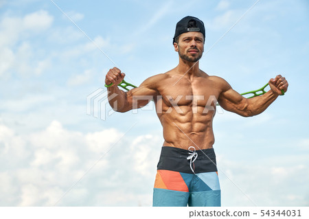 Man with bare chest pulling silicons expander by hands. 54344031
