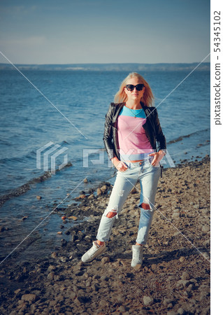 Beautiful blonde in ripped jeans posing on the shore of the blue sea 54345102