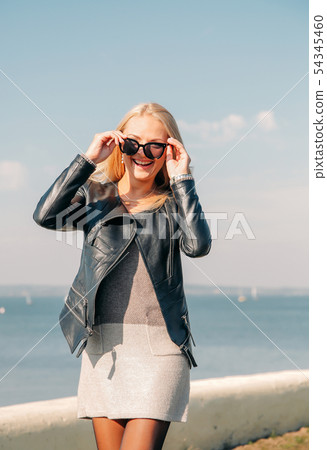 Beautiful blonde in black sunglasses posing on the shore of the blue sea Beautiful blonde in black sunglasses posing on the shore of the blue sea 54345460