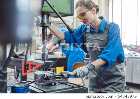 Metal worker woman operating drilling machine 54345979
