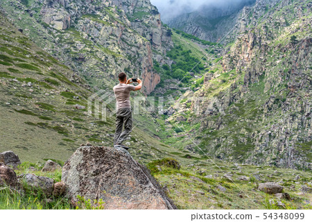 Male hiker takes photo of beautiful mountains in North Caucasus in summer 54348099
