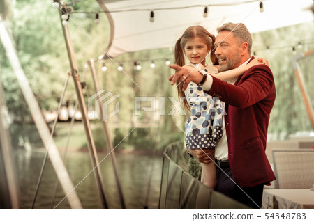 Father holding his daughter while looking at ducks in lake 54348783