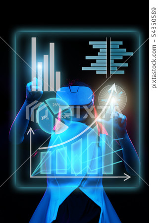 Woman uses a virtual reality headset to work with data in the form of graphs and charts. Woman uses a virtual reality headset to work with data in the form of graphs and charts. 54350589
