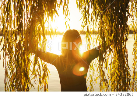 Autumn portrait of young girl with willow branches on the background of a lake at sunset 54352865