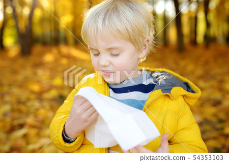 Little boy sneezing and wipes nose with napkin Little boy sneezing and wipes nose with napkin 54353103