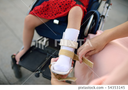 Mother puts on orthosis her daughter legs. Mother puts on orthosis her daughter legs. 54353145