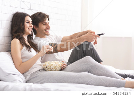 Man and woman in love watching film with popcorn in bed 54354124