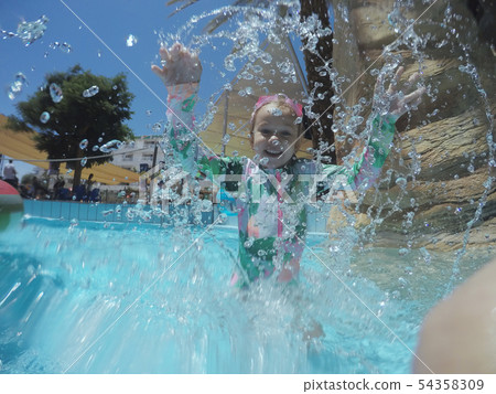 Little girl playing and spraying water in swimming pool outdoors at summer 54358309