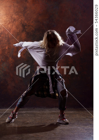 Photo of young dancing blonde girl in ripped jeans and sneakers on dark brown background Photo of young dancing blonde girl in ripped jeans and sneakers on dark brown background 54366029