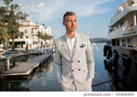 Handsome businessman is wearing white fashion costume stands on the background of the bay with Handsome businessman is wearing white fashion costume stands on the background of the bay with 54368484