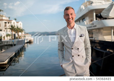 Handsome businessman is wearing white fashion costume stands on the background of the bay with 54368485