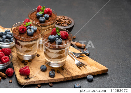 Classic tiramisu dessert with blueberries and raspberries in a glass on wooden cutting board on dark 54368672