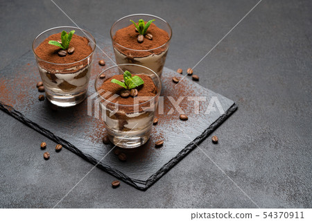 Classic tiramisu dessert in a glass on stone serving board on dark concrete background 54370911