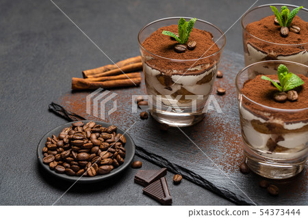 Classic tiramisu dessert in a glass on stone serving board on dark concrete background Classic tiramisu dessert in a glass on stone serving board on dark concrete background 54373444