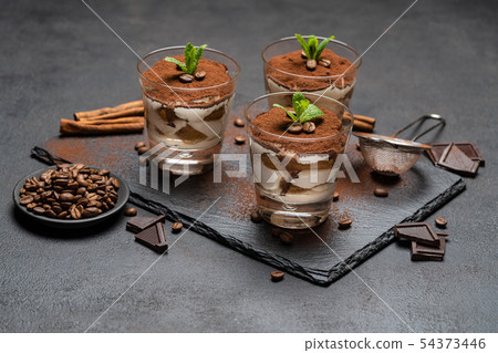 Classic tiramisu dessert in a glass on stone serving board on dark concrete background Classic tiramisu dessert in a glass on stone serving board on dark concrete background 54373446