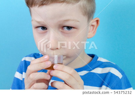 boy takes medicine syrup on blue background boy takes medicine syrup on blue background 54375232