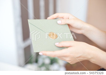 Close-up photo of female hands holding a silver blue or pink invitation envelope with a wax seal, a Close-up photo of female hands holding a silver blue or pink invitation envelope with a wax seal, a 54375320