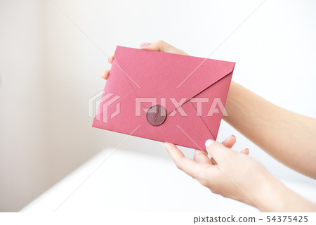 Close-up photo of female hands holding a silver invitation envelope with a wax seal, a gift 54375425