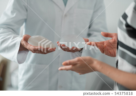 Plastic surgeon wearing white lab coat holding implants for breast Plastic surgeon wearing white lab coat holding implants for breast 54375818