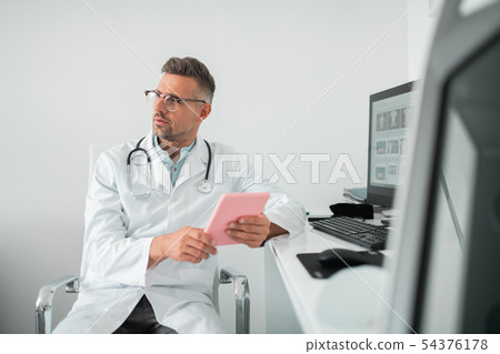 Bearded handsome plastic surgeon sitting in his modern clinic 54376178