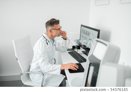 Plastic surgeon wearing stethoscope on neck working on computer Plastic surgeon wearing stethoscope on neck working on computer 54376185