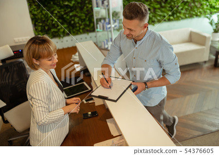 Handsome businessman smiling while talking to administrator at clinic Handsome businessman smiling while talking to administrator at clinic 54376605