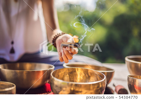 Woman playing on Tibetan singing bowl while sitting on yoga mat against a waterfall. Vintage tonned Woman playing on Tibetan singing bowl while sitting on yoga mat against a waterfall. Vintage tonned 54384770