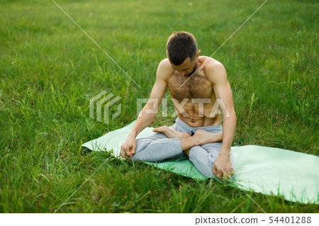 Young man practicing yoga on green grass 54401288