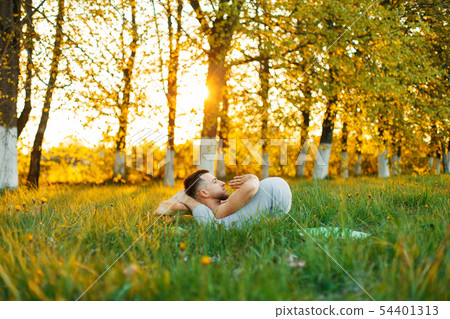 man practicing yoga in the park at sunset.  54401313