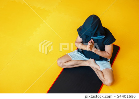 Man in hood doing yoga in a gym on a black mat  54401686