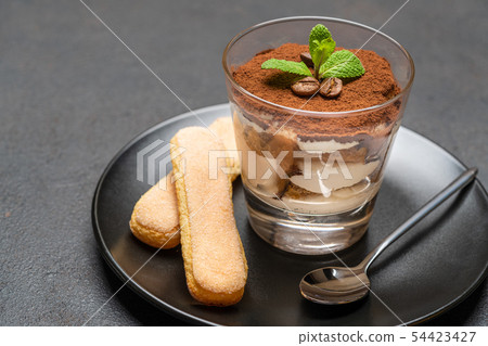 Classic tiramisu dessert in a glass and savoiardi cookies on dark concrete background Classic tiramisu dessert in a glass and savoiardi cookies on dark concrete background 54423427