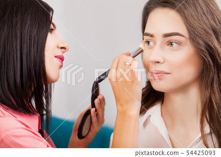Professional makeup artist working with beautiful young woman Professional makeup artist working with beautiful young woman 54425093