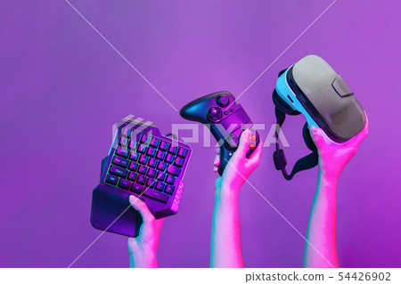 Set of hands with gamepad, keyboard, virtual reality headset and headphones on violet background. 54426902
