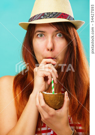 Woman wearing a a swimsuit and straw hat drinks coconaut milk over colorful turquoise background Woman wearing a a swimsuit and straw hat drinks coconaut milk over colorful turquoise background 54427893