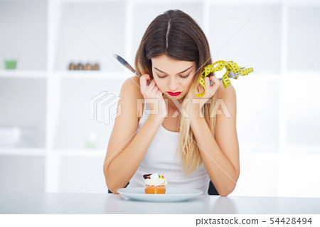 Diet. Woman hungry girl with yellow measuring tape holds in hand cake cupcake. Weight loss dieting 54428494