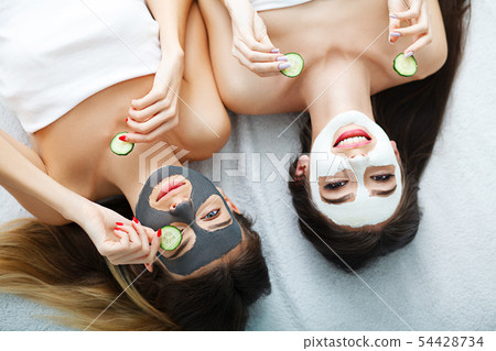 Portrait of two beautiful girls with facial cream on their faces looking at the camera and lying 54428734