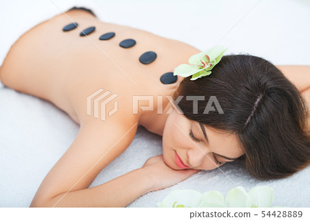 Beautiful woman relaxing in spa salon with hot stones on body. 54428889