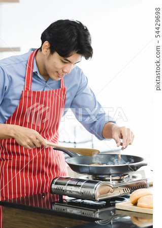 Asian man fried hamburger in pan on stove.. Asian man fried hamburger in pan on stove.. 54429698