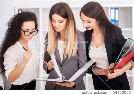 Team portrait of happy businesswomen standing on office corridor, looking at camera, smiling. 54430060