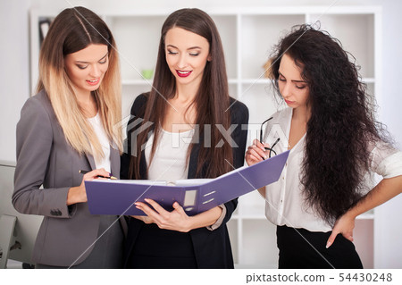 Team portrait of happy businesswomen standing on office corridor, looking at camera, smiling. 54430248