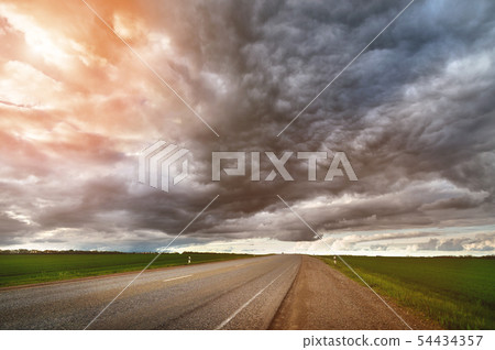 Evening landscape of suburban asphalt road with low textured dramatic clouds and green fields on the 54434357