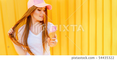 Outdoor fashion portrait of young hipster girl with ice-cream on yellow wall background 54435322
