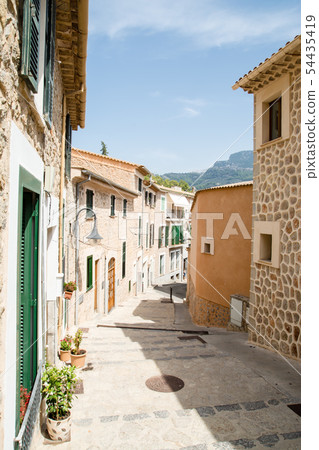 Majorca's cityscape A pale-marooned wall and stone-walled houses with windows with cobblestone alleys and plants with green dark doors 54435419