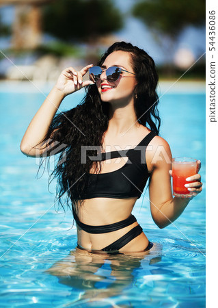 Tenned beautiful woman in orange bikini and sunlasses sitting in swimming pool with cocktail Tenned beautiful woman in orange bikini and sunlasses sitting in swimming pool with cocktail 54436086