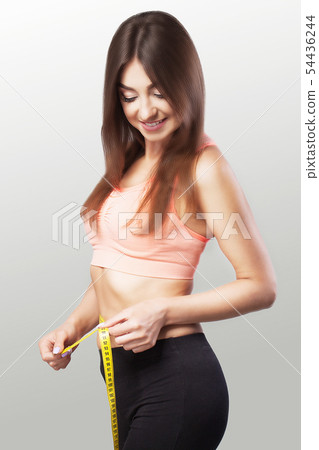 Slender girl. Hands to measure the waist tape. Fit and healthy woman on a gray background. The 54436244